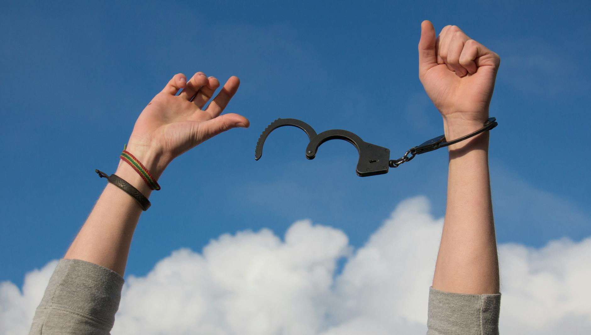 Hands breaking free from handcuffs against the open sky, symbolizing freedom from dependence and reclaiming self-sovereignty.